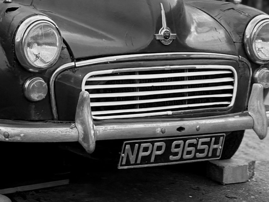 The grille, headlamps and winged Morris badge of a Morris Minor 1000 in black and white
